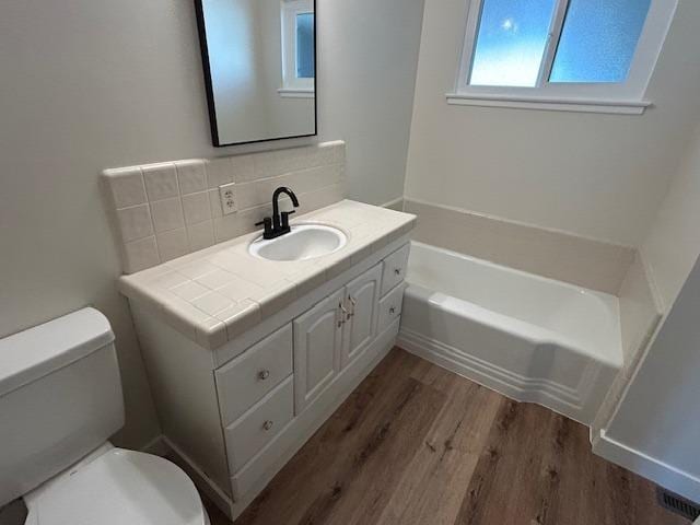 bathroom with hardwood / wood-style floors, vanity, a bath, backsplash, and toilet