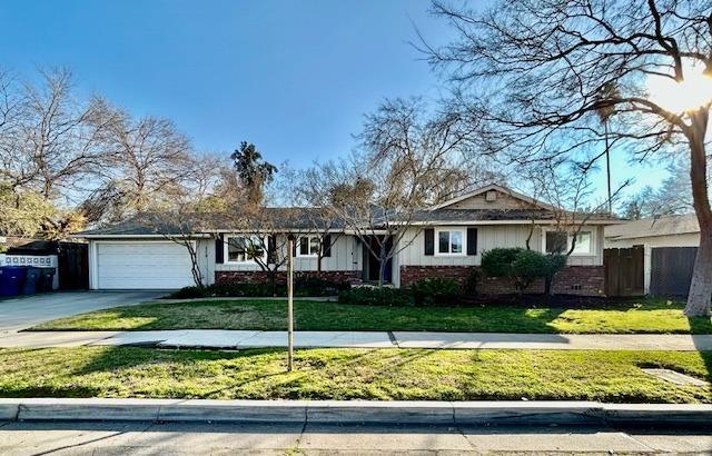 ranch-style home with an attached garage, driveway, fence, and a front lawn