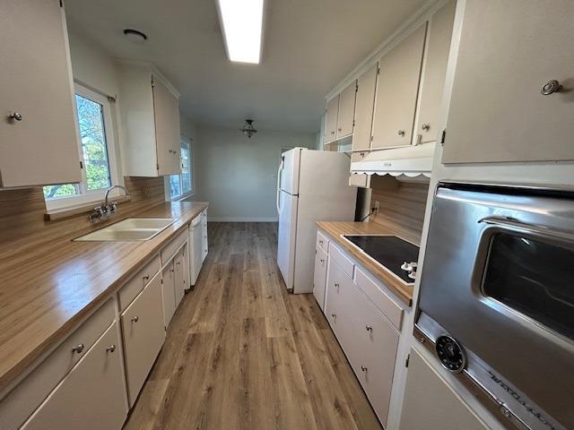 kitchen featuring backsplash, black electric stovetop, sink, light wood-type flooring, and white cabinetry