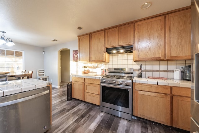 kitchen featuring tile countertops, an inviting chandelier, decorative backsplash, dark hardwood / wood-style floors, and stainless steel range with gas stovetop