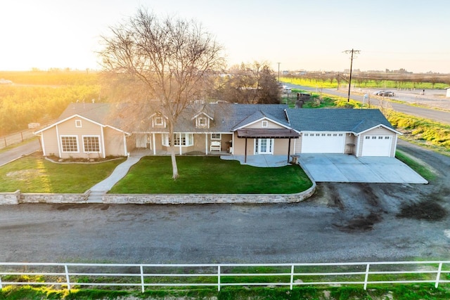 view of front of home with covered porch, a rural view, a garage, and a yard