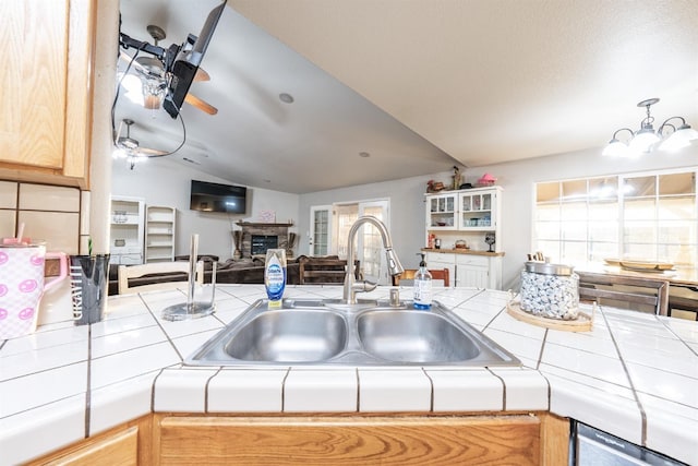 kitchen featuring a stone fireplace, tile counters, lofted ceiling, and sink