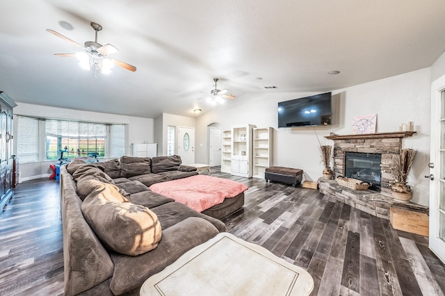 living room featuring vaulted ceiling, dark hardwood / wood-style floors, a stone fireplace, and ceiling fan