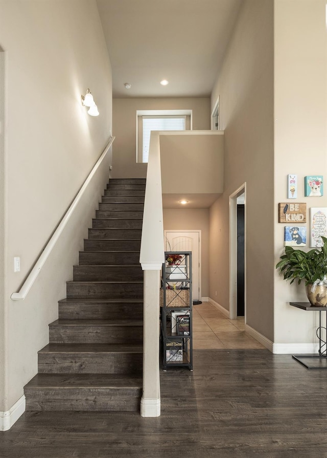 stairway with wood-type flooring and a towering ceiling