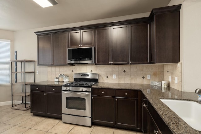 kitchen with appliances with stainless steel finishes, dark brown cabinetry, sink, dark stone countertops, and light tile patterned flooring