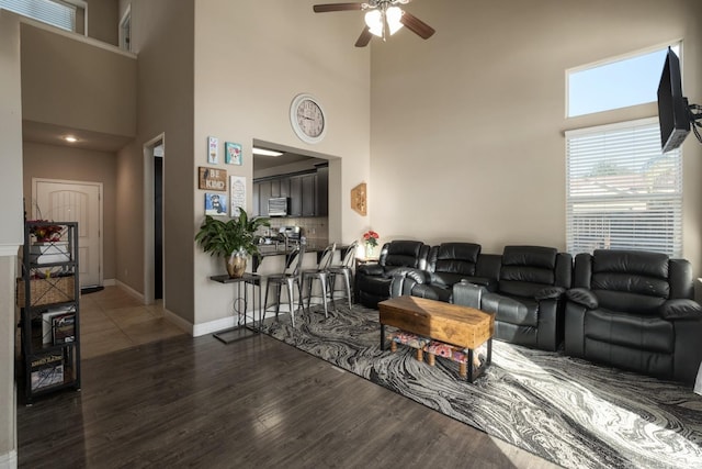 living room with a towering ceiling, dark hardwood / wood-style flooring, and ceiling fan