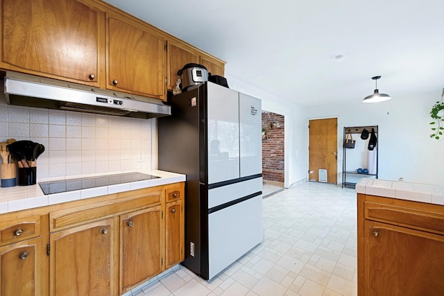 kitchen with black electric stovetop, backsplash, pendant lighting, stainless steel refrigerator, and tile counters