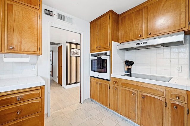 kitchen with tile countertops, oven, black electric cooktop, and tasteful backsplash