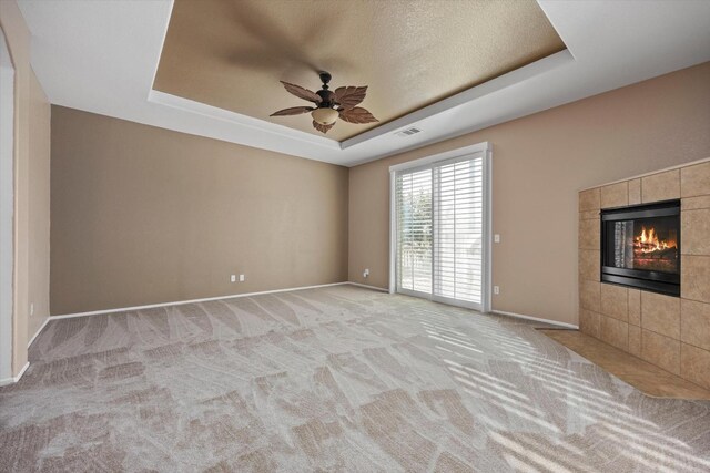 unfurnished room with a tile fireplace, ceiling fan, a raised ceiling, a textured ceiling, and light carpet