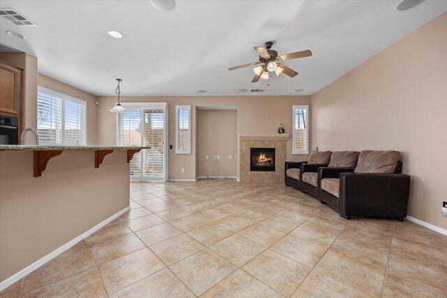 tiled living room with a tile fireplace and ceiling fan