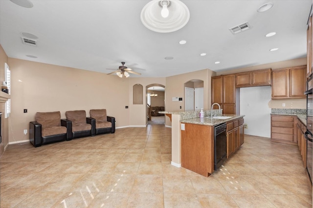 kitchen featuring ceiling fan, light stone countertops, sink, black dishwasher, and an island with sink