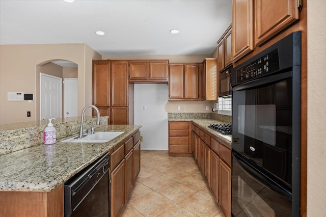 kitchen with light stone counters, black appliances, sink, light tile patterned floors, and a center island with sink