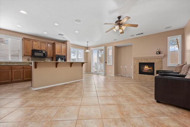 kitchen featuring light stone countertops, pendant lighting, a kitchen bar, a tiled fireplace, and black appliances