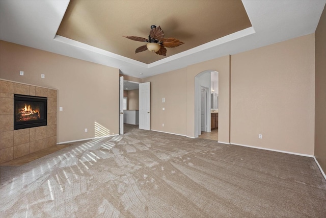 unfurnished living room featuring light carpet, a tray ceiling, ceiling fan, and a tiled fireplace