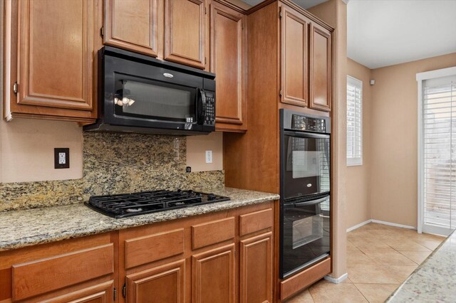 kitchen with tasteful backsplash, light stone counters, light tile patterned floors, and black appliances