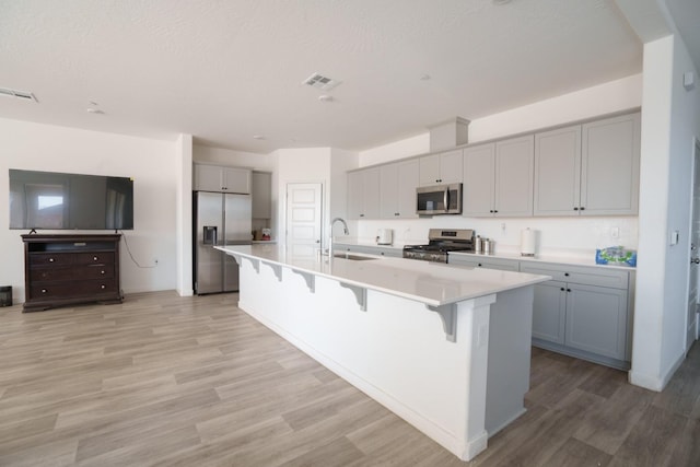 kitchen featuring sink, stainless steel appliances, a large island with sink, gray cabinets, and a breakfast bar