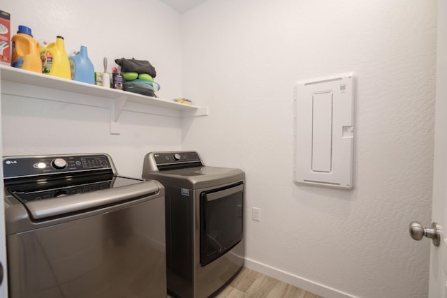 laundry area with electric panel, light hardwood / wood-style floors, and independent washer and dryer