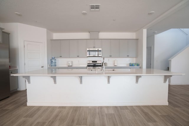 kitchen with gray cabinetry, a breakfast bar, sink, appliances with stainless steel finishes, and a large island