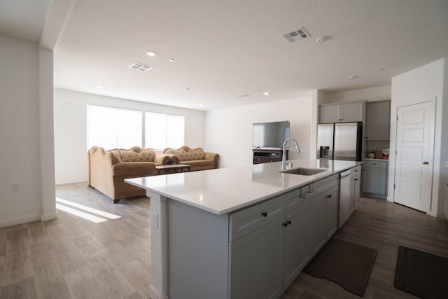 kitchen featuring gray cabinetry, stainless steel fridge with ice dispenser, a center island with sink, and sink