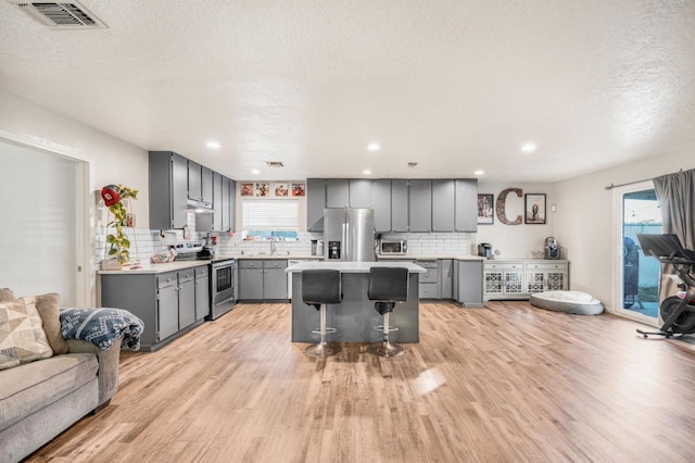 kitchen with appliances with stainless steel finishes, a kitchen bar, gray cabinets, a kitchen island, and light wood-type flooring