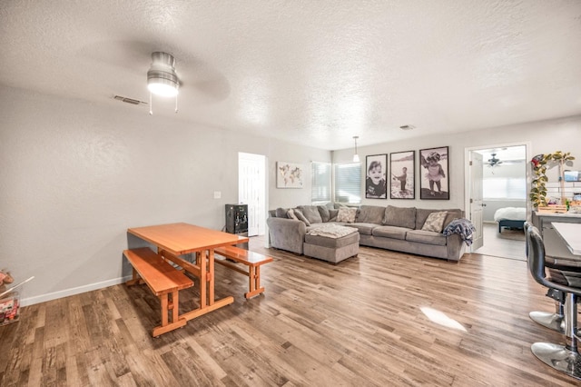 living room with ceiling fan, a textured ceiling, and light wood-type flooring