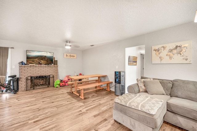 living room featuring a textured ceiling, light hardwood / wood-style flooring, and a brick fireplace