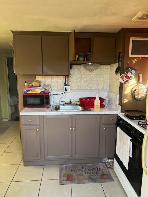 kitchen with decorative backsplash, light tile patterned floors, range with gas cooktop, and sink