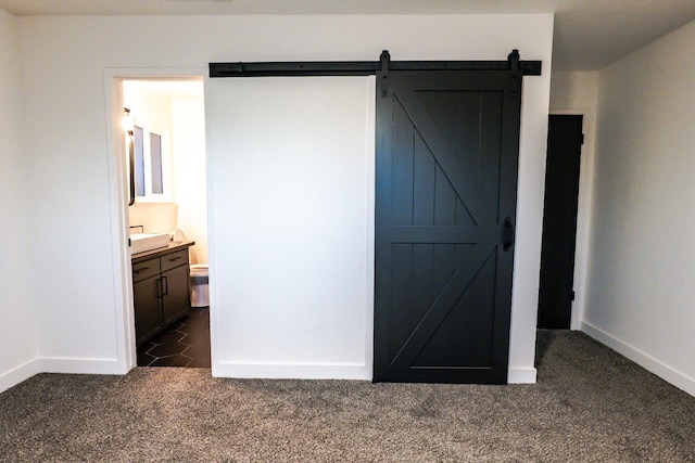 unfurnished bedroom featuring ensuite bathroom, dark colored carpet, and a barn door