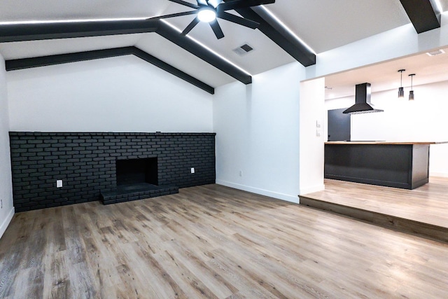 unfurnished living room featuring hardwood / wood-style floors, lofted ceiling with beams, a brick fireplace, and ceiling fan