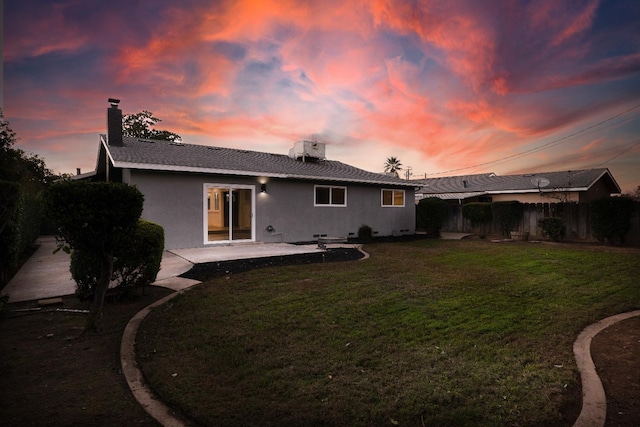 back house at dusk featuring a yard and a patio