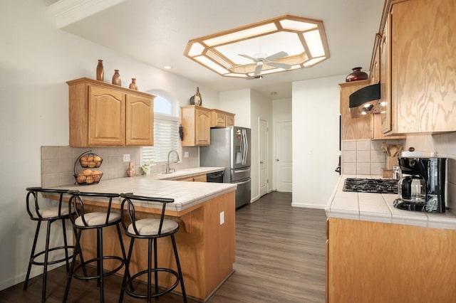 kitchen featuring kitchen peninsula, ceiling fan, exhaust hood, sink, and tile counters