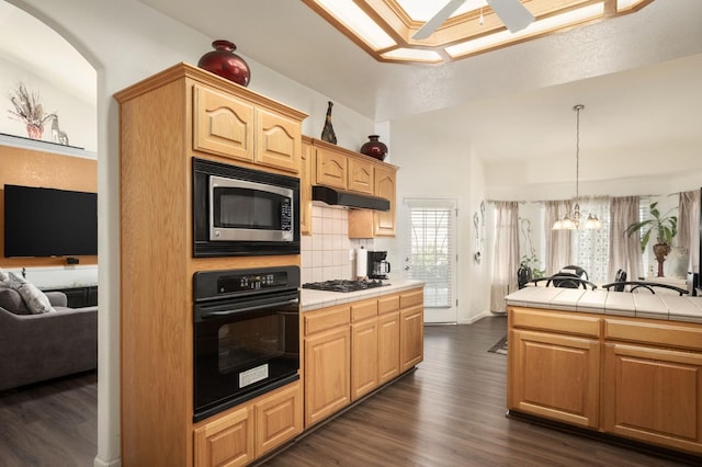 kitchen with tasteful backsplash, light brown cabinets, tile counters, black oven, and stainless steel microwave