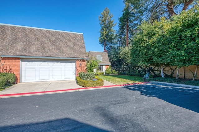 exterior space featuring roof with shingles, concrete driveway, a garage, and brick siding