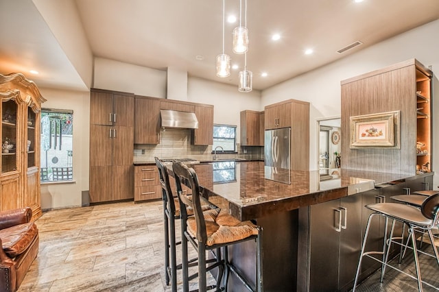 kitchen featuring a kitchen bar, stainless steel appliances, hanging light fixtures, and range hood