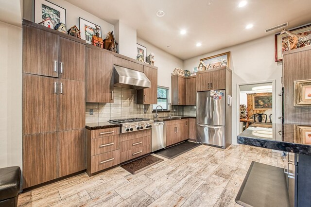 kitchen with recessed lighting, backsplash, wall chimney exhaust hood, stainless steel appliances, and a sink