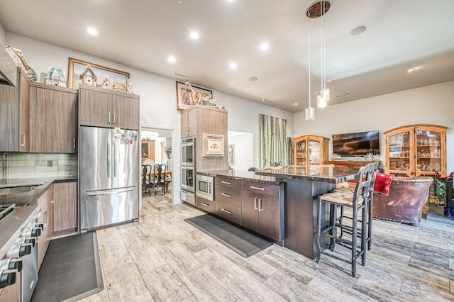 kitchen featuring visible vents, appliances with stainless steel finishes, a breakfast bar, dark stone counters, and decorative backsplash