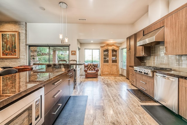 kitchen with decorative backsplash, stainless steel appliances, pendant lighting, light hardwood / wood-style flooring, and range hood