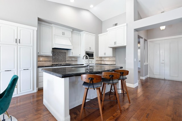 kitchen featuring sink, custom exhaust hood, white cabinetry, a center island with sink, and stainless steel microwave