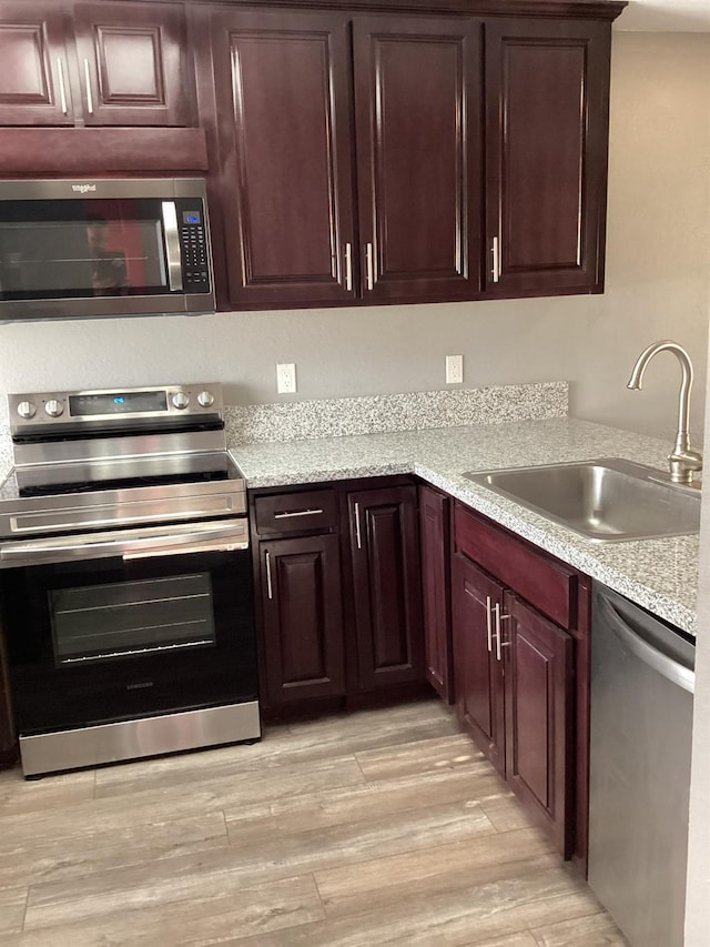 kitchen with light stone counters, sink, stainless steel appliances, and light wood-type flooring