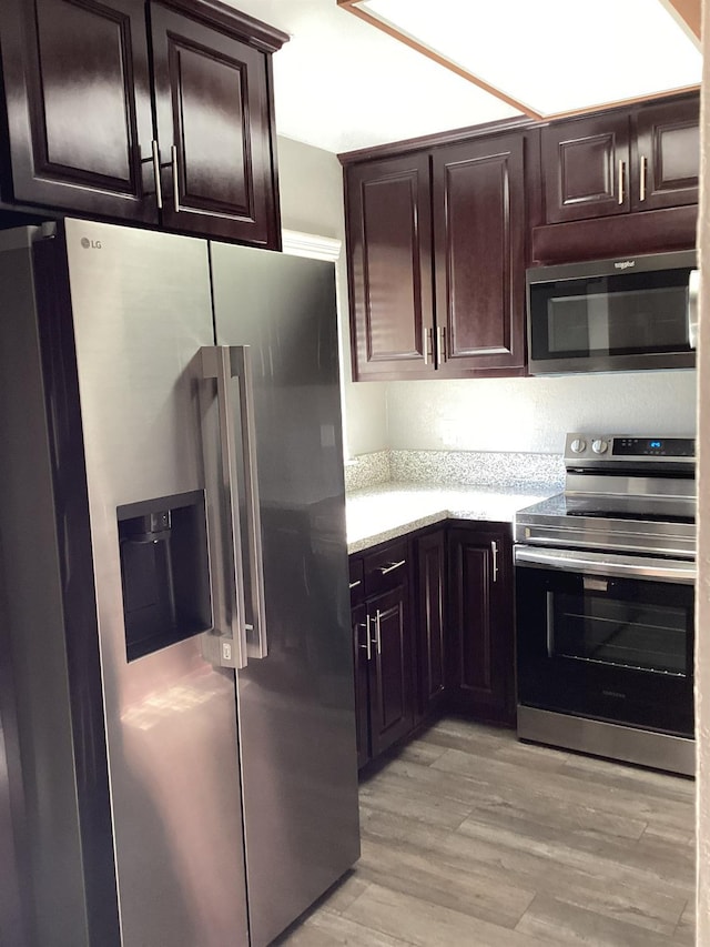 kitchen with dark brown cabinetry, light hardwood / wood-style flooring, and appliances with stainless steel finishes