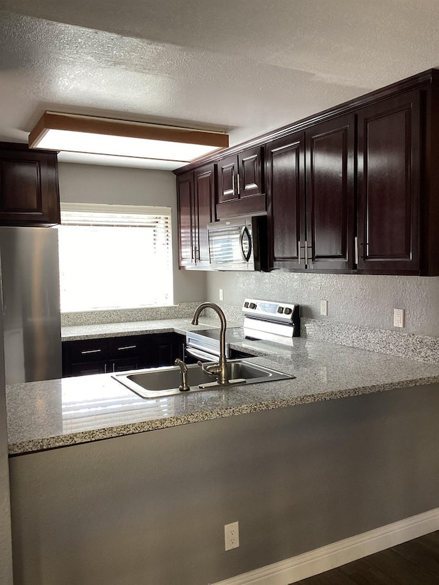 kitchen with stainless steel fridge, light stone countertops, sink, and a textured ceiling