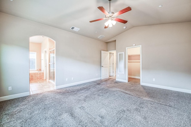 unfurnished bedroom with lofted ceiling, a walk in closet, ceiling fan, light carpet, and ensuite bath