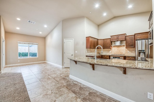 kitchen with sink, appliances with stainless steel finishes, high vaulted ceiling, light stone countertops, and a kitchen bar