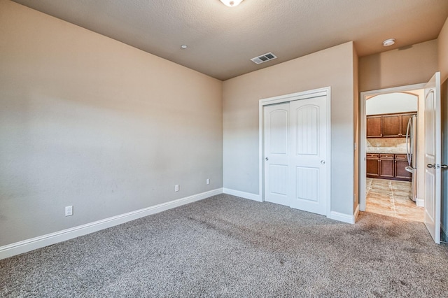 unfurnished bedroom featuring a closet, stainless steel fridge, light carpet, and a textured ceiling