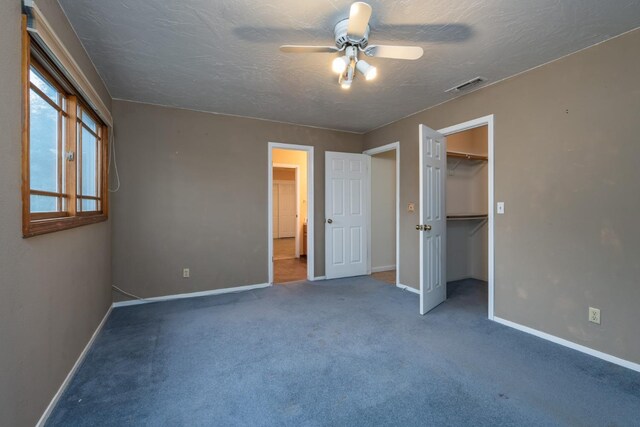 unfurnished bedroom with a walk in closet, a textured ceiling, a closet, ceiling fan, and carpet