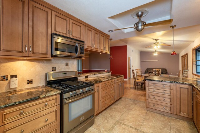 kitchen with tasteful backsplash, hanging light fixtures, appliances with stainless steel finishes, ceiling fan, and dark stone counters