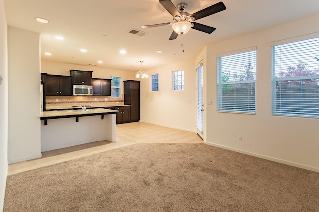 kitchen featuring a kitchen bar, light carpet, backsplash, ceiling fan with notable chandelier, and hanging light fixtures