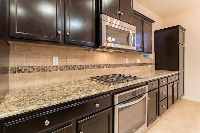 kitchen featuring light stone countertops, stainless steel appliances, decorative backsplash, dark brown cabinets, and light tile patterned flooring