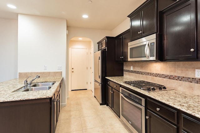 kitchen featuring light stone countertops, backsplash, stainless steel appliances, and sink