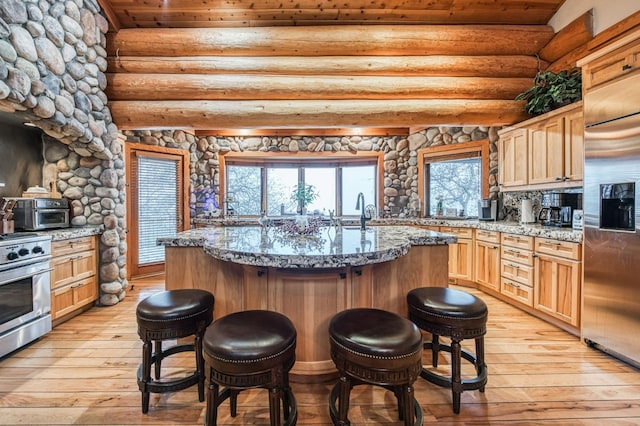 12755 Rusty Spur Ln, Clovis, CA 93619 - kitchen featuring appliances with stainless steel finishes, a breakfast bar, light wood-style floors, light stone counters, and rustic walls